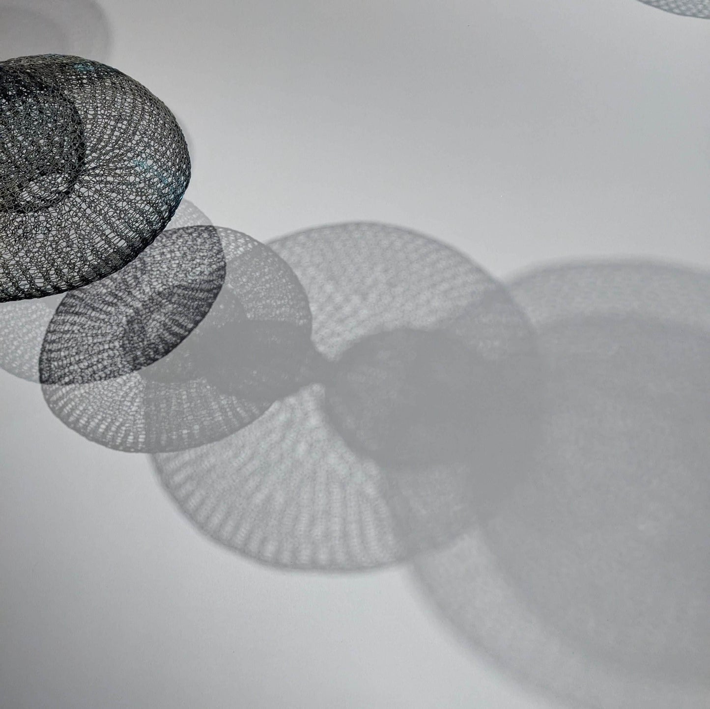 A series of circular metal mesh objects casting intricate shadows on a white surface, creating an abstract visual effect.