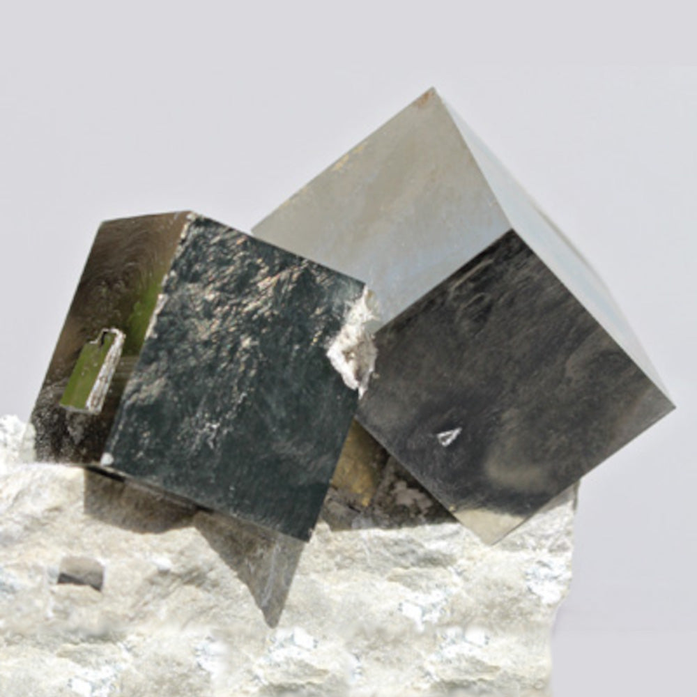 Two reflective cubic crystals, one dark and one light, resting on a textured white mineral base, showcasing their geometric shapes.