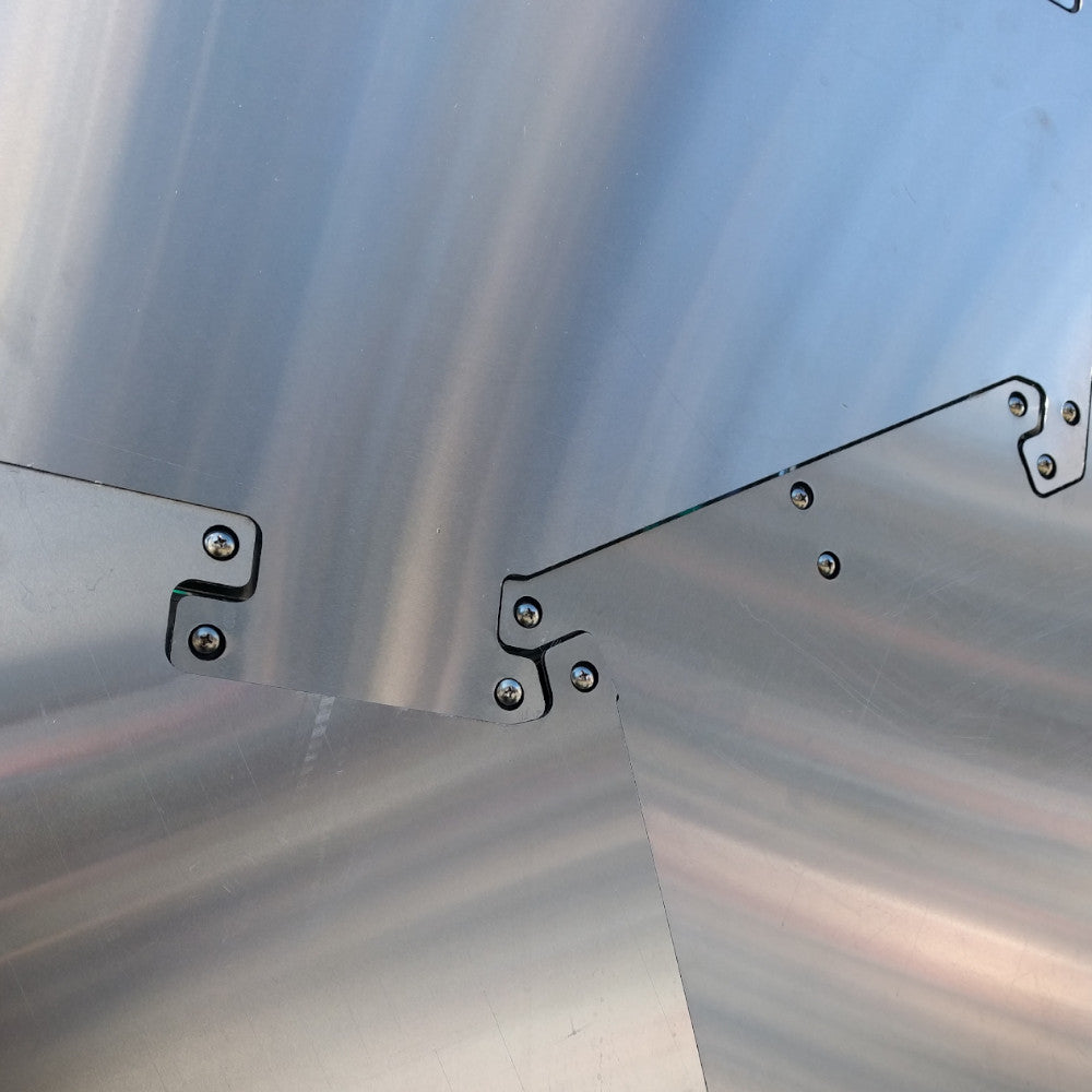 Close-up of polished metal plates with precise cut-outs and screws, showcasing intricate design and angular joins in a shiny finish.