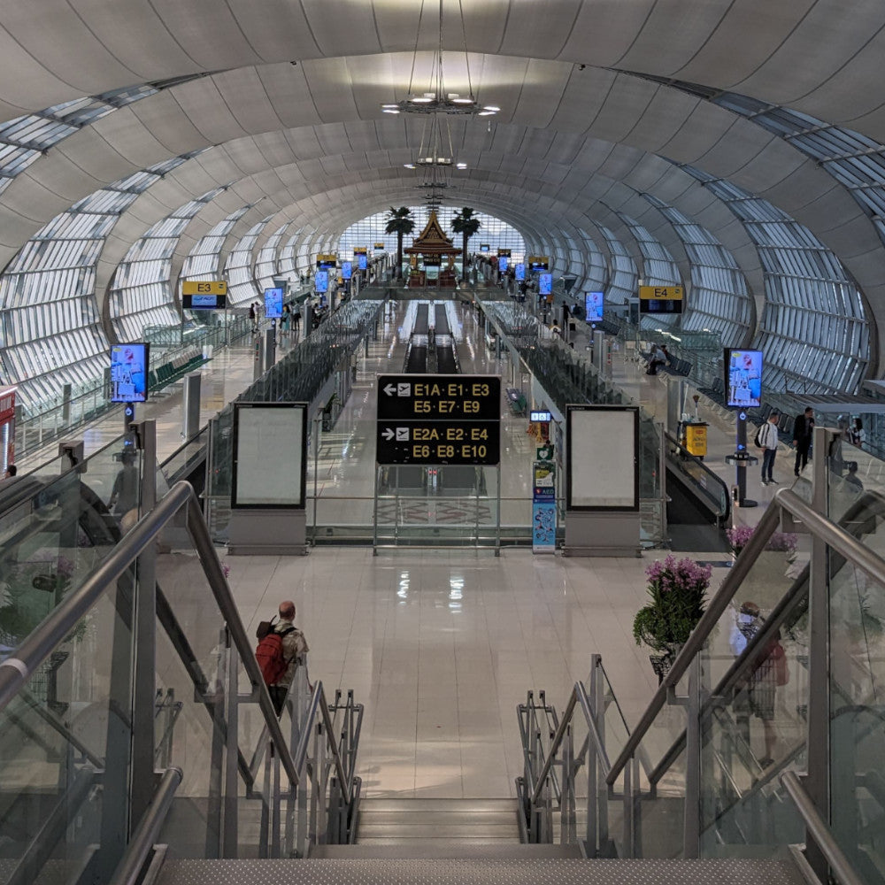 Interior view of a modern airport terminal, showcasing sleek architecture, illuminated signs, and travelers moving along the concourse.