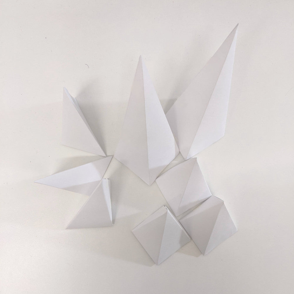 Eight white paper pyramids sitting on a white surface.