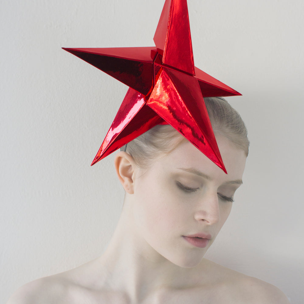 A headpiece made from five shiny red pyramids sits on the head of a woman in front of a white background. 