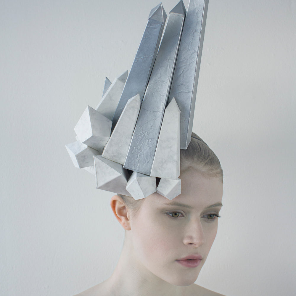 White and silver obelisks shoot up from a headpiece worn by a woman in front of a white background. 