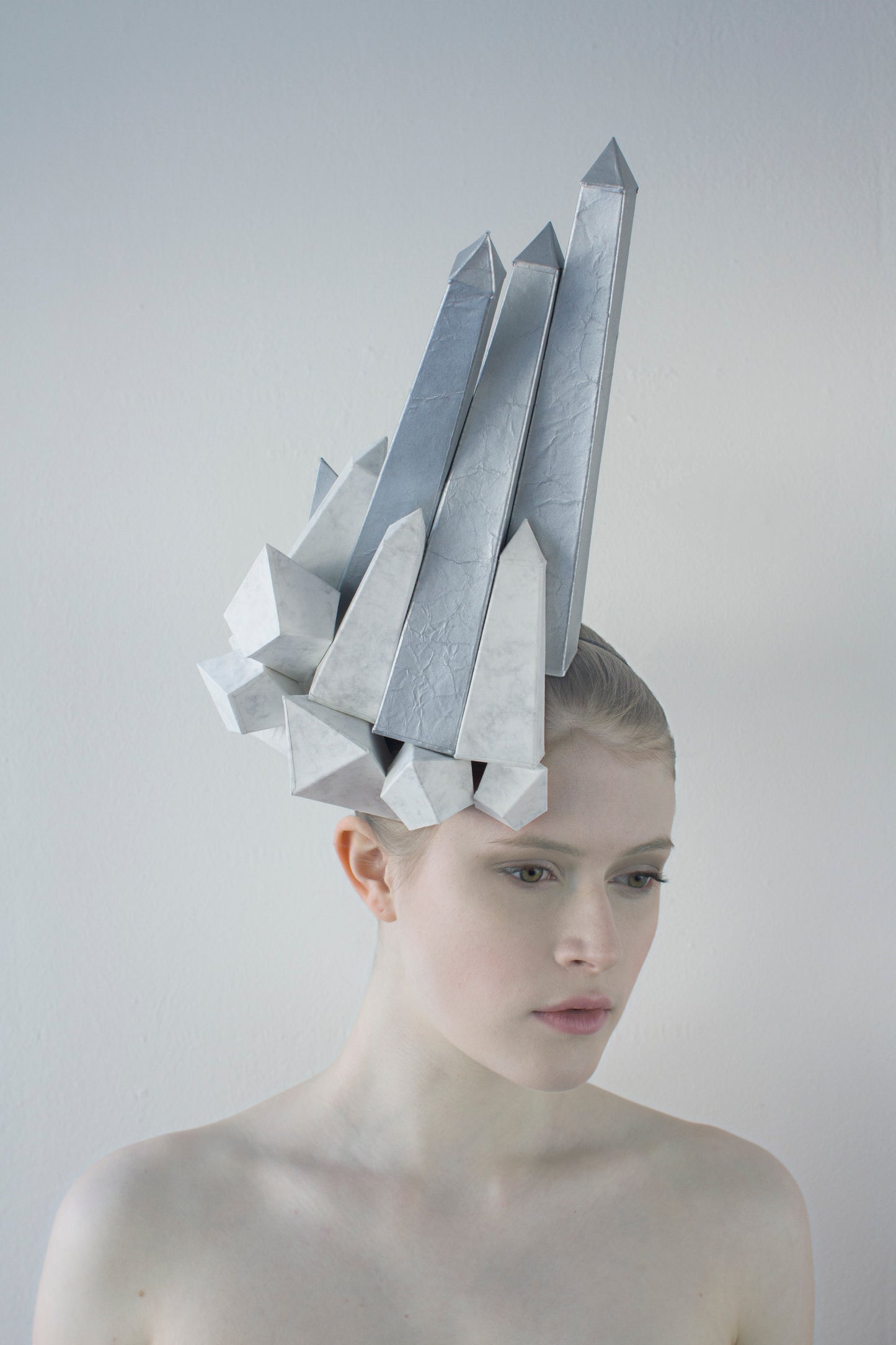 White and silver obelisks shoot up from a headpiece worn by a woman in front of a white background. 