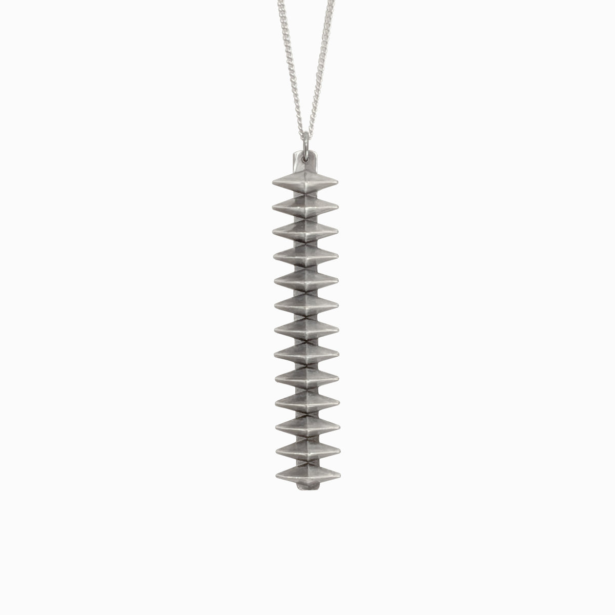 A vertical, textured silver pendant with a tiered design, suspended from a delicate chain against a white background.