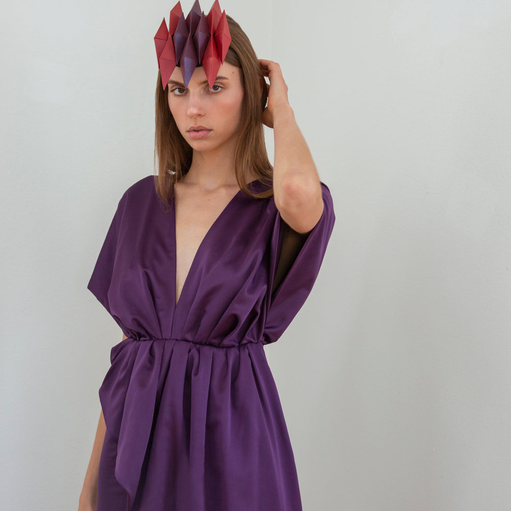 
                  
                    A woman with long brown hair wearing a purple dress and headpiece with ten red and purple pyramids. 
                  
                