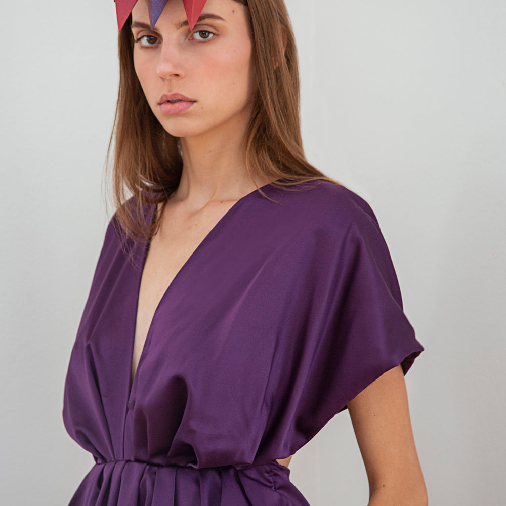 
                  
                    A woman with long brown hair wearing a purple dress and headpiece with ten red and purple pyramids. 
                  
                