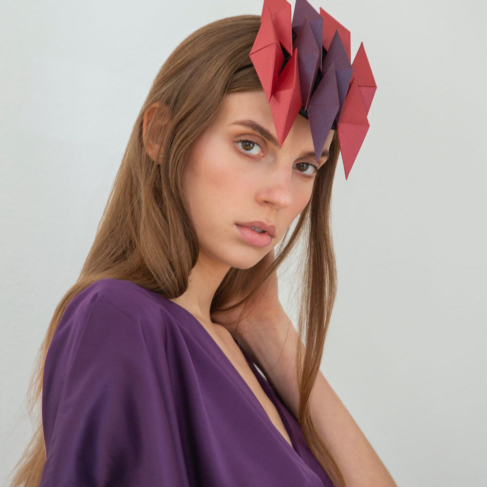 
                  
                    A woman with long brown hair wearing a purple dress and headpiece with ten red and purple pyramids. 
                  
                