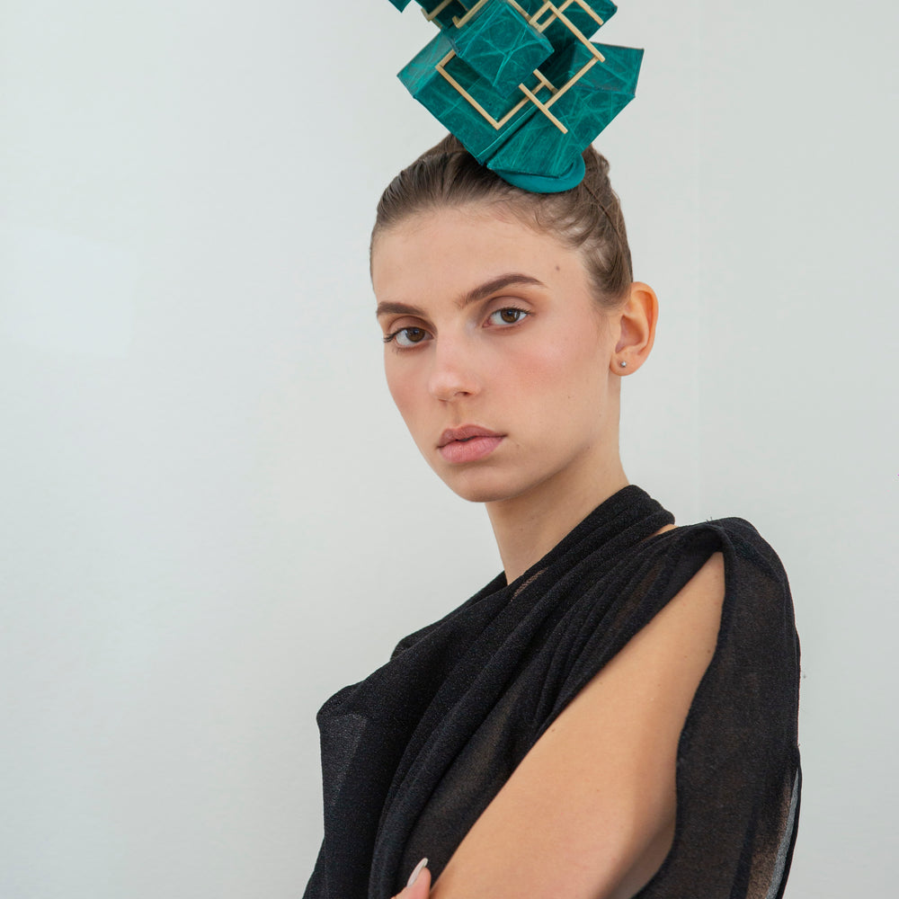 A woman wearing a black dress is wearing a green headpiece made from a pile of cubes. 
