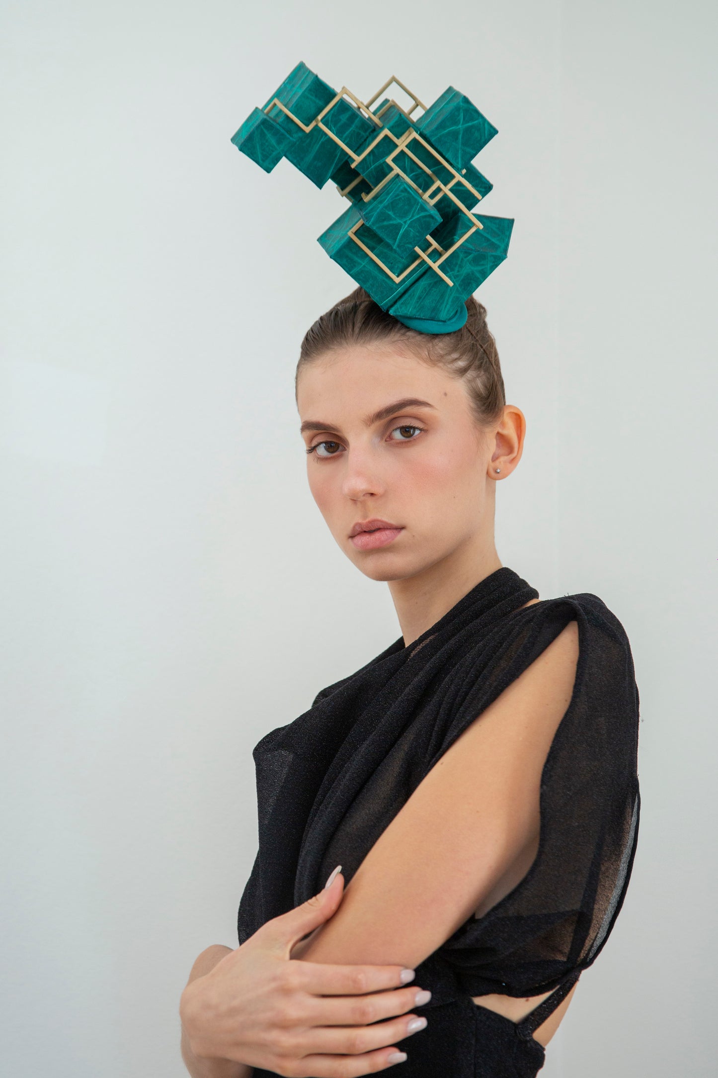 A woman wearing a black dress is wearing a green headpiece made from a pile of cubes. 