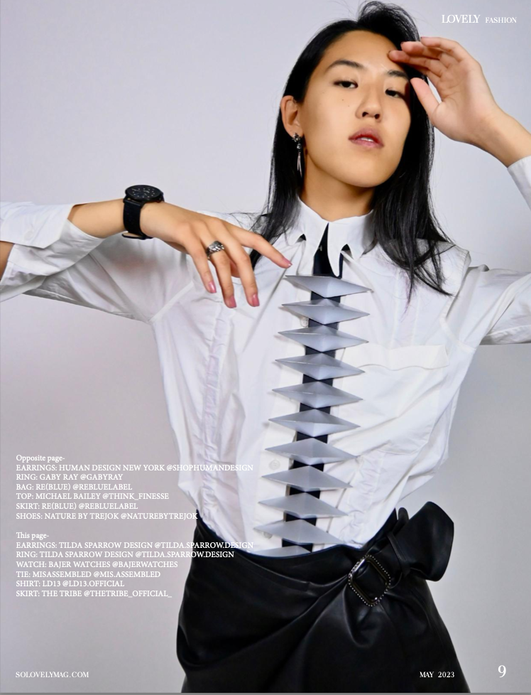 A model showcases a striking white shirt with a long dramatic necklace, paired with a black skirt and accessories.