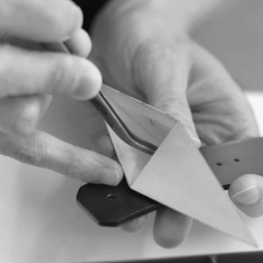 A person delicately holds a metal tool against a black piece, focusing on precision in a crafting process.