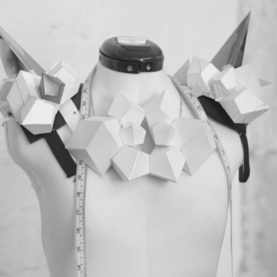 An abstract design on a mannequin's shoulders featuring geometric white shapes, spikes, and a measuring tape draped down.