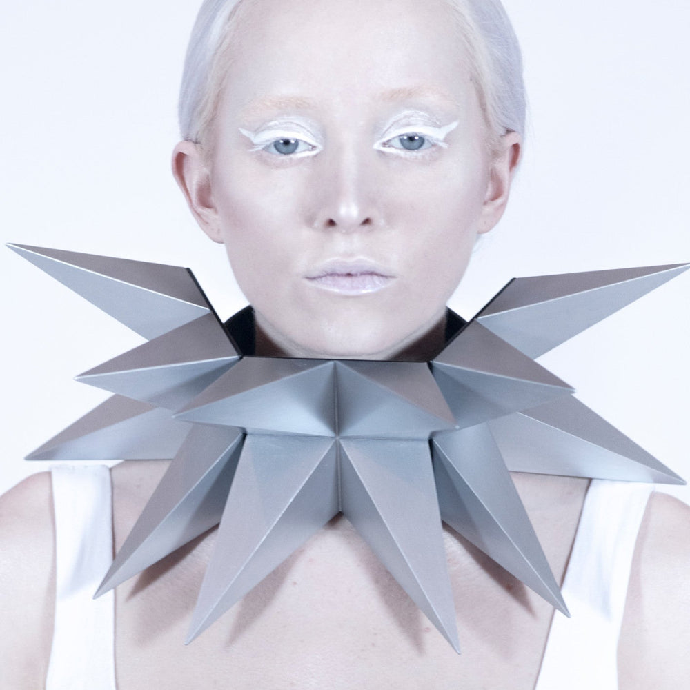 
                  
                    A pale woman wearing an oversized necklace that has twelve large silver pyramids.
                  
                