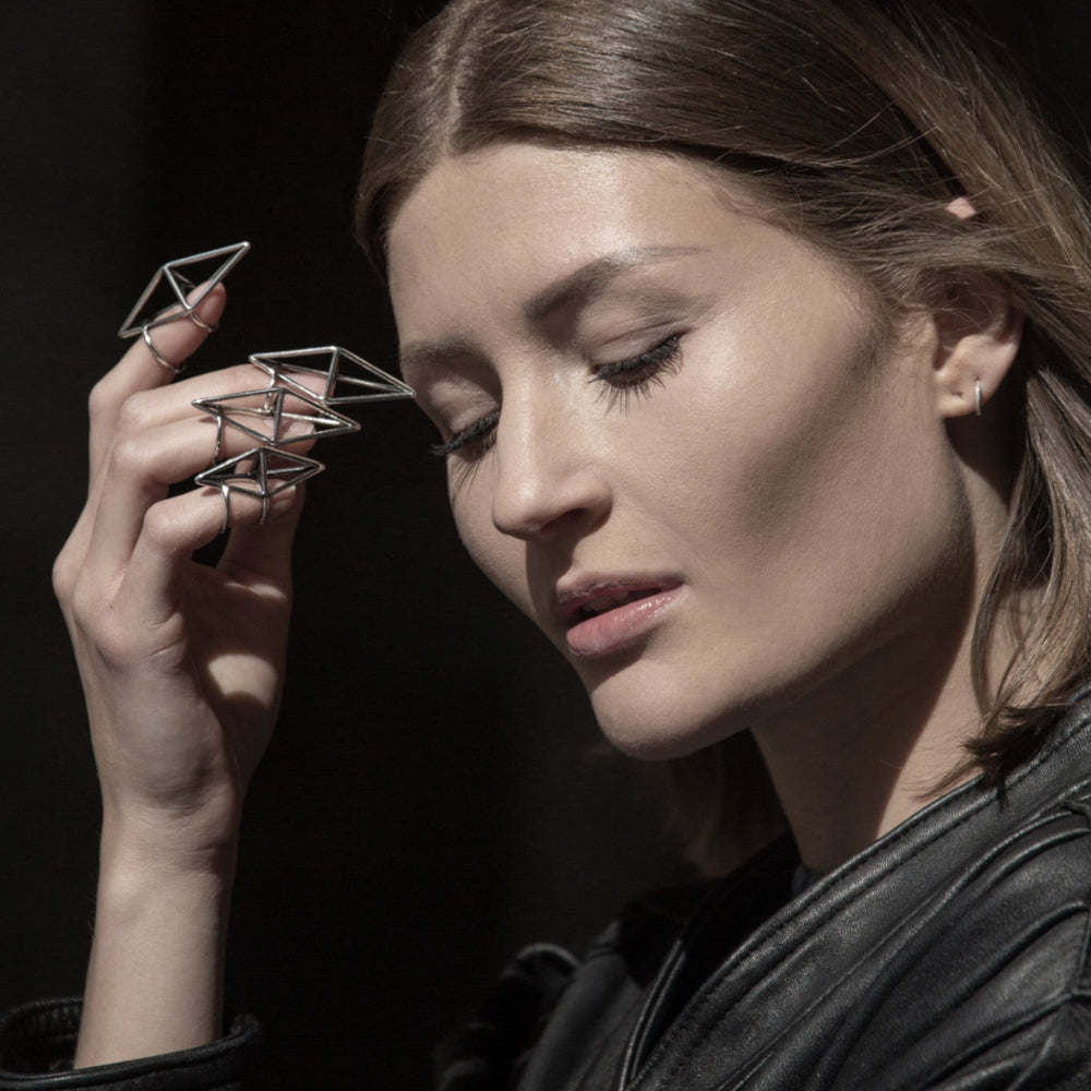 A hand adorned with geometric metal rings poses against a dark background, showcasing modern, artistic jewelry design.