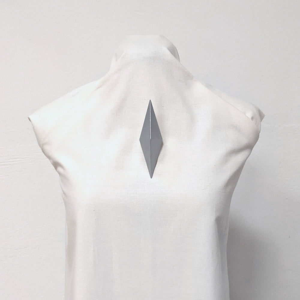 
                  
                    A close-up of a white mannequin displaying a sleek, gray, diamond-shaped brooch pinned to its back.
                  
                