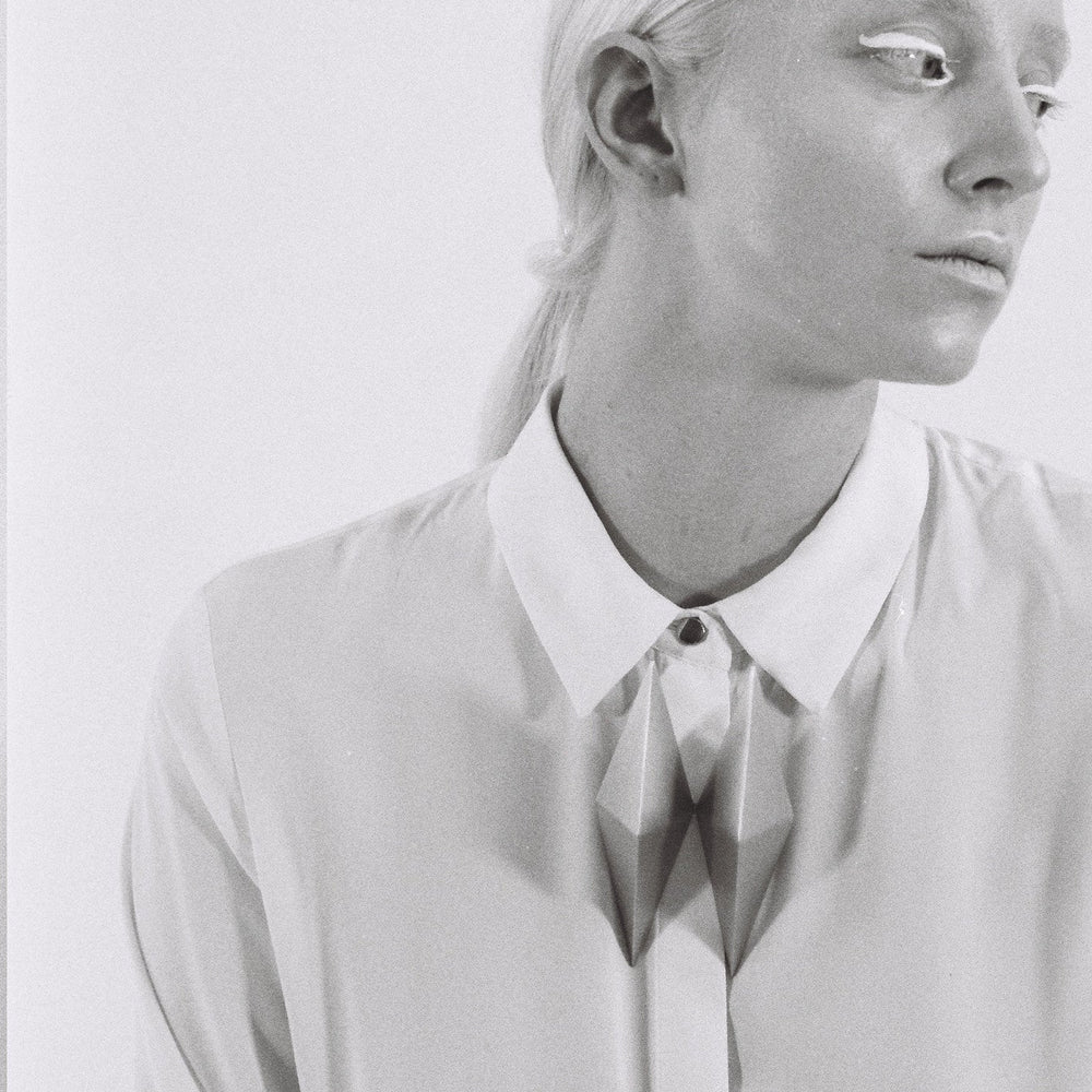 A close-up of a person wearing a pristine white shirt with a geometric design and a buttoned collar, set against a plain backdrop.