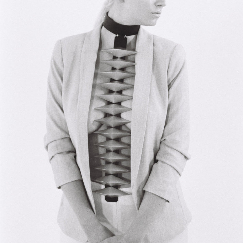 A person in a tailored light-colored blazer with a unique, structured cutout design on the torso area, styled against a minimalist background.