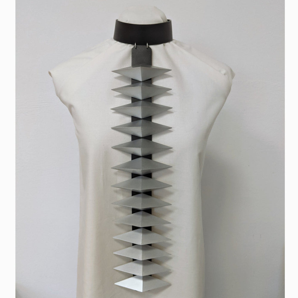 
                  
                    A fashion design on a mannequin features a unique gray and black statement necklace with layered, triangular elements.
                  
                