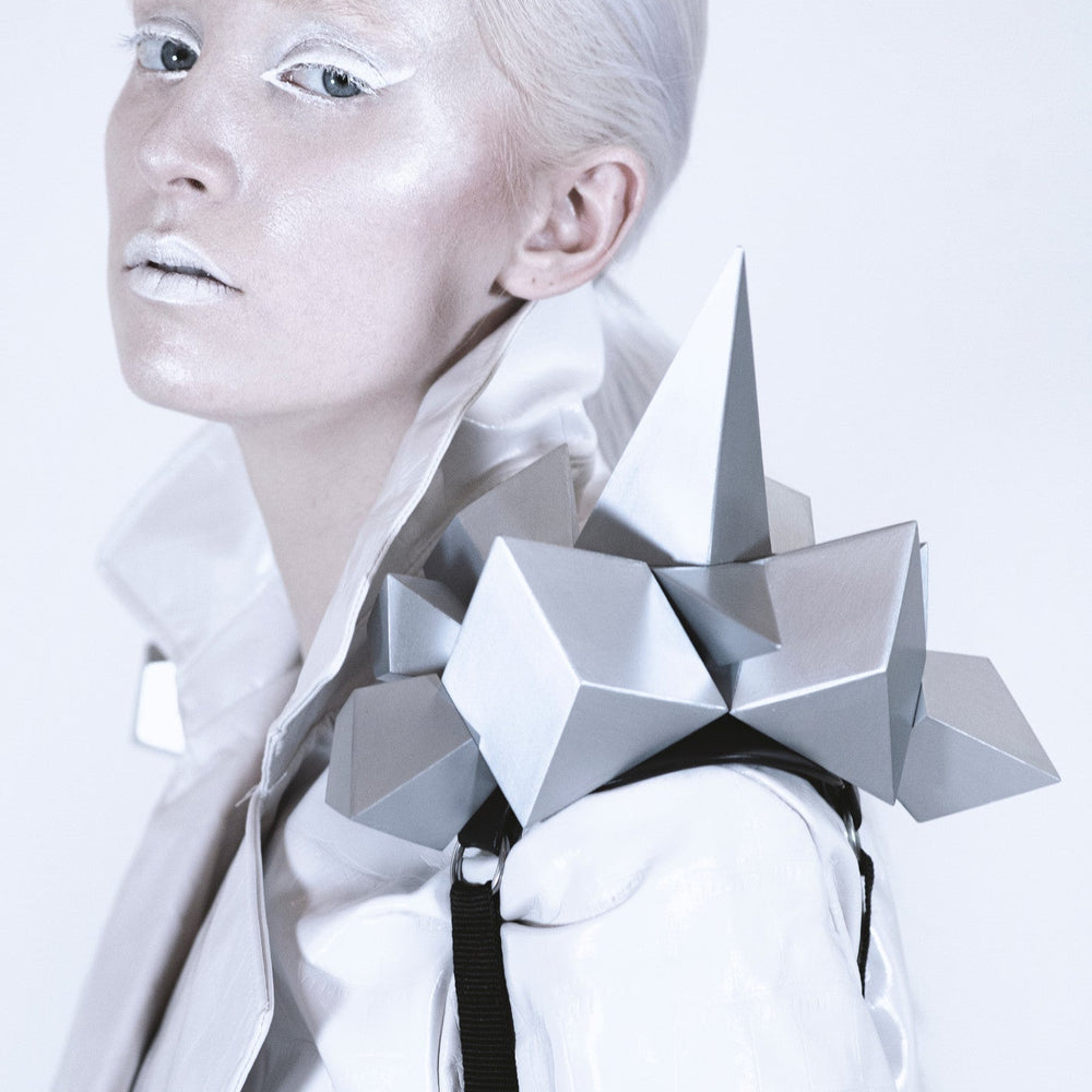 A futuristic fashion design featuring a person wearing a sleek white jacket adorned with silver geometric shapes on the shoulder.