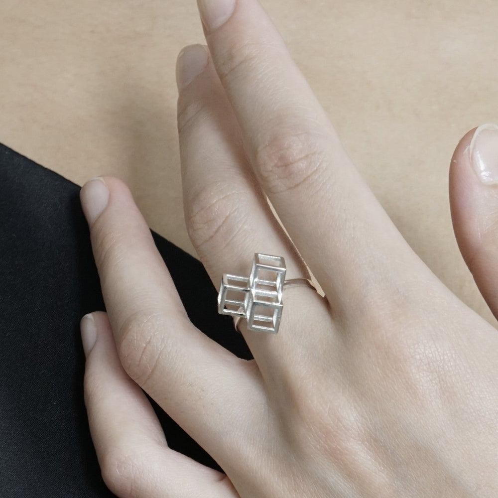 
                  
                    A hand wearing a modern silver ring featuring a cubic design, showcased against a neutral background.
                  
                