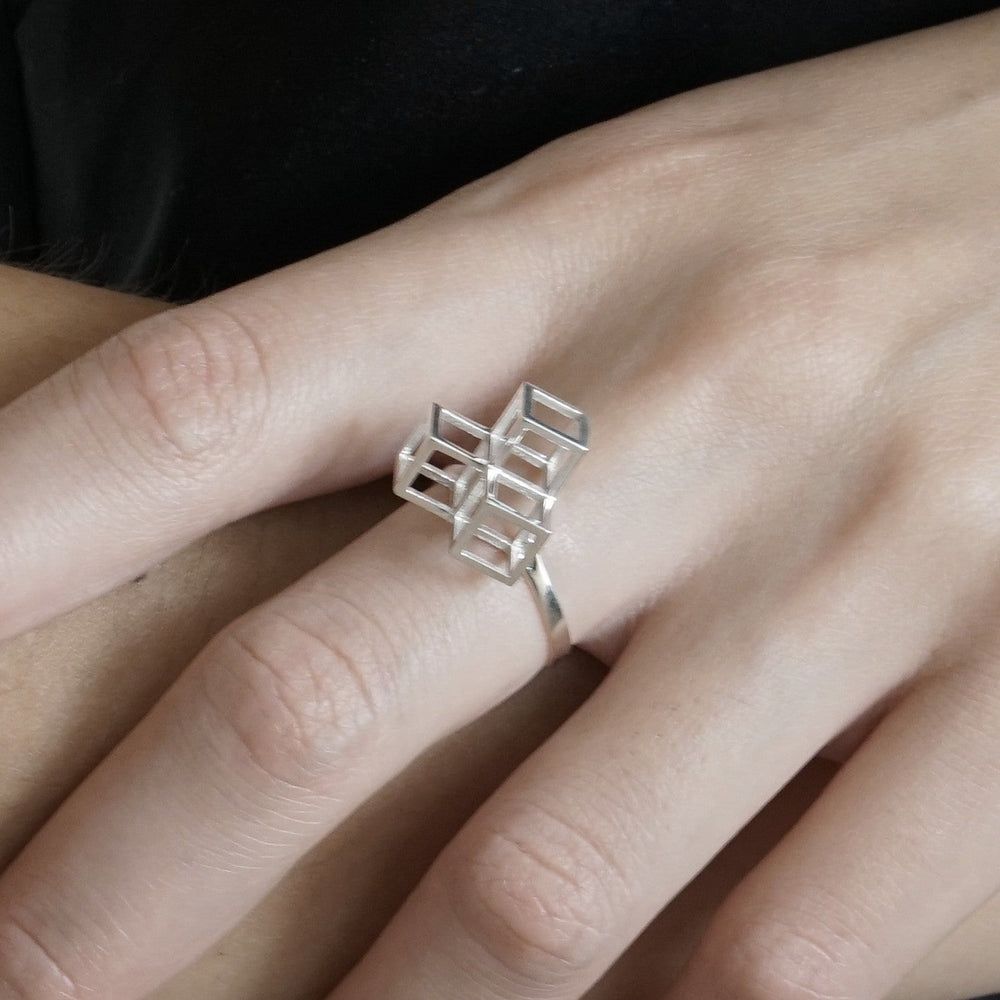 
                  
                    A close-up of a hand wearing a modern silver ring featuring an abstract geometric design with interlocking cube shapes.
                  
                
