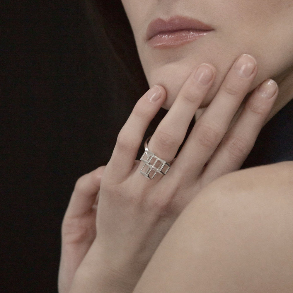
                  
                    A close-up of a woman's hand with a geometric silver ring, gently resting her chin against her fingers, highlighting elegant jewelry.
                  
                