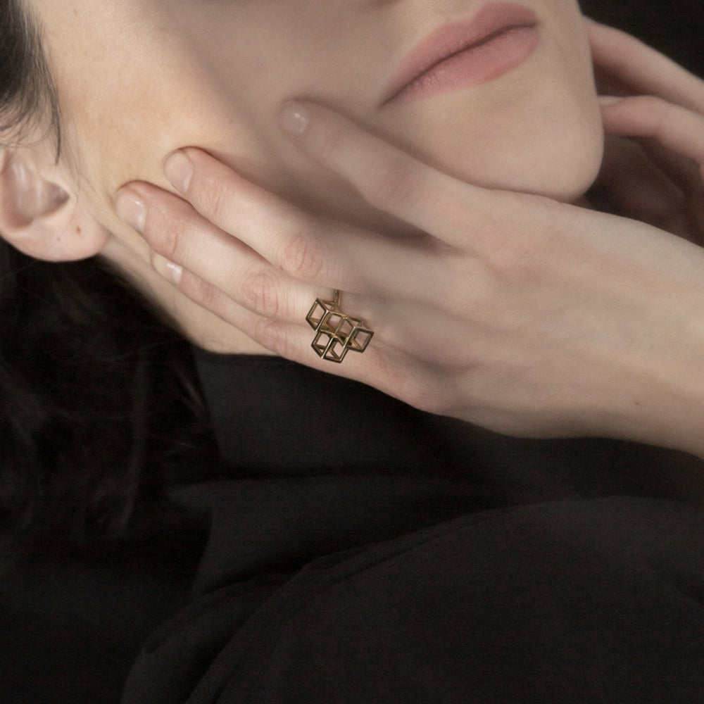 
                  
                    A close-up of a woman with soft makeup, gently touching her face, showcasing a geometric gold ring on her finger.
                  
                