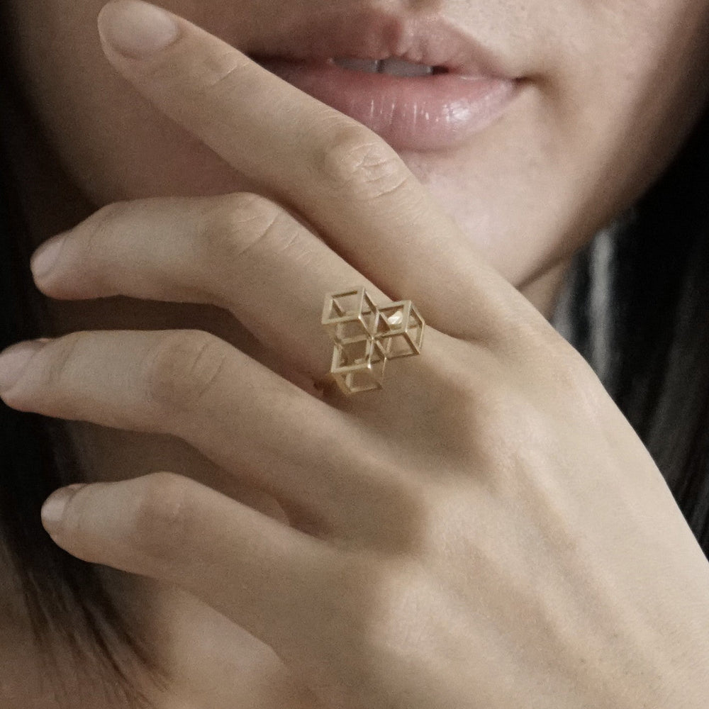 
                  
                    A woman’s hand gracefully holds her face, showcasing a unique geometric gold ring on her finger.
                  
                