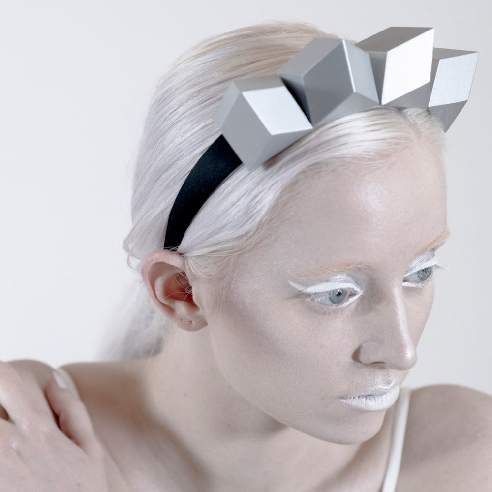 A person with sleek, straight platinum hair wears a geometric silver headband against a minimalist white background.