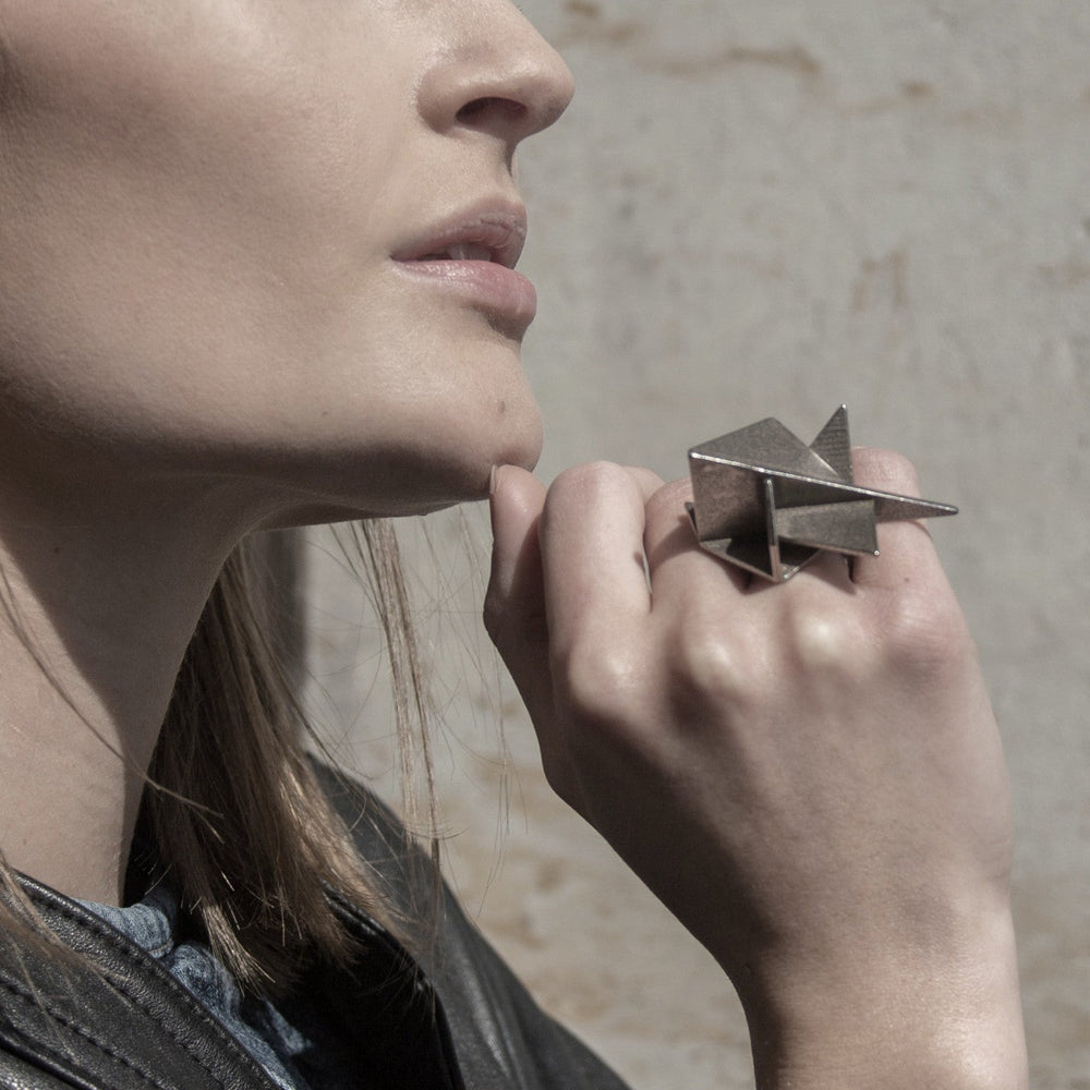 A close-up of a hand displaying a unique geometric silver ring, with the person’s hair and leather jacket partially visible.