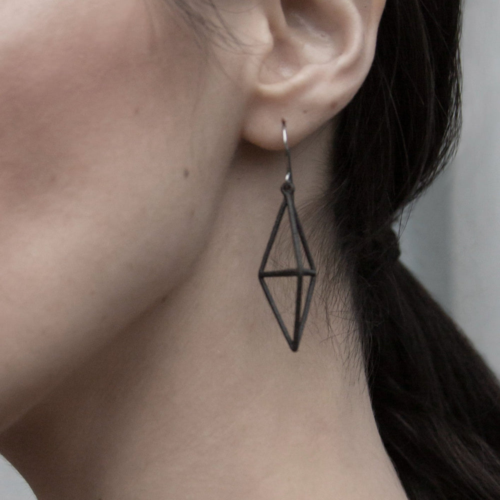 
                  
                    Close-up of a woman's ear showcasing a stylish, geometric black hoop earring that adds a modern touch to her look.
                  
                