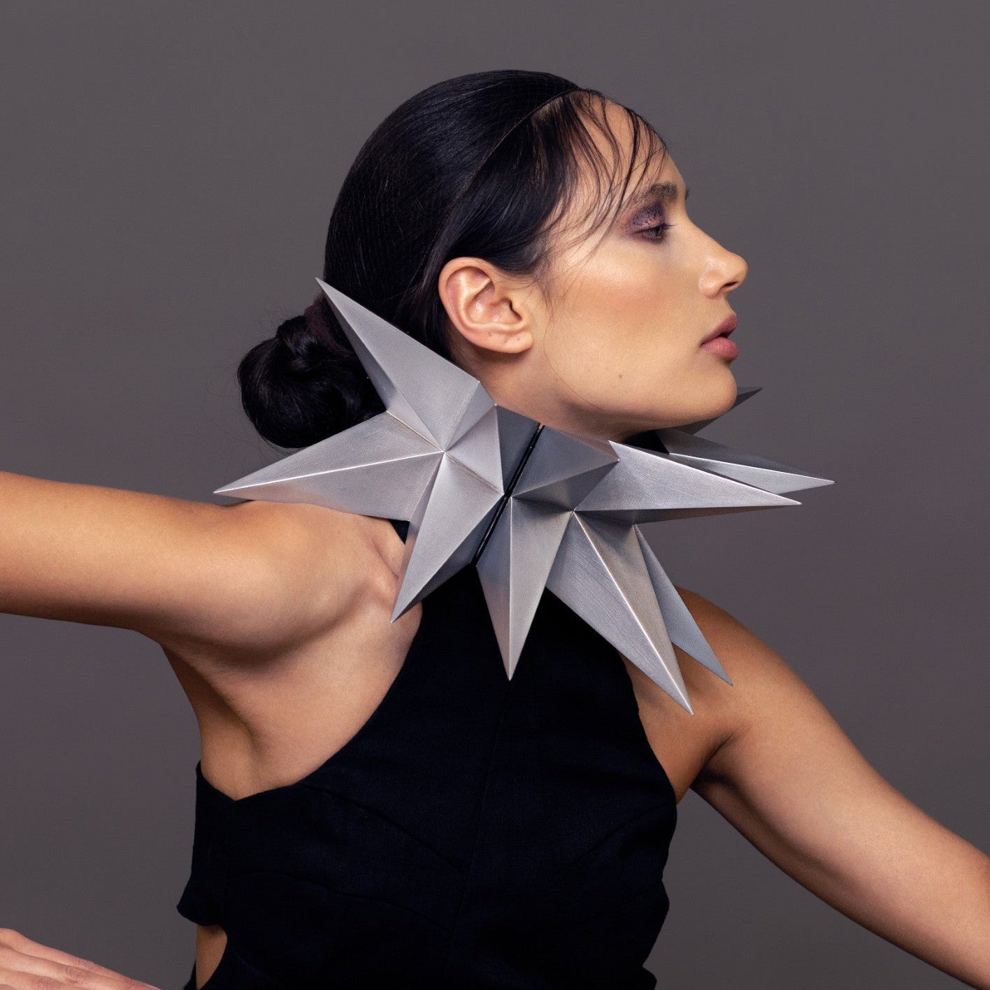 A model showcases a striking silver star-shaped collar, contrasting against a black outfit and a neutral background.