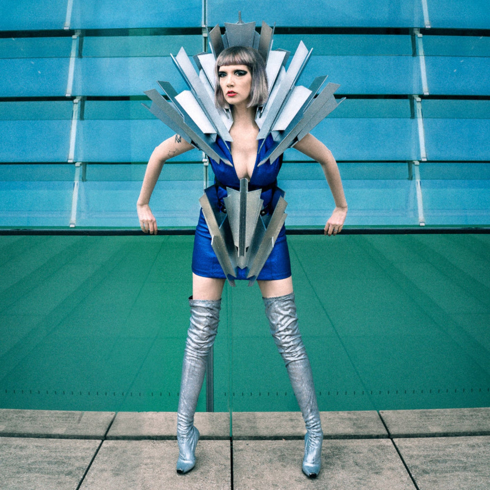 A person poses dramatically in a metallic, futuristic outfit, featuring a striking angular design and thigh-high silver boots.