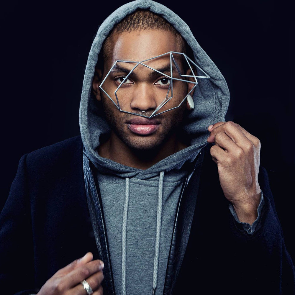 A person wearing a grey hoodie under a black jacket, standing against a dark background, showcasing casual urban style.