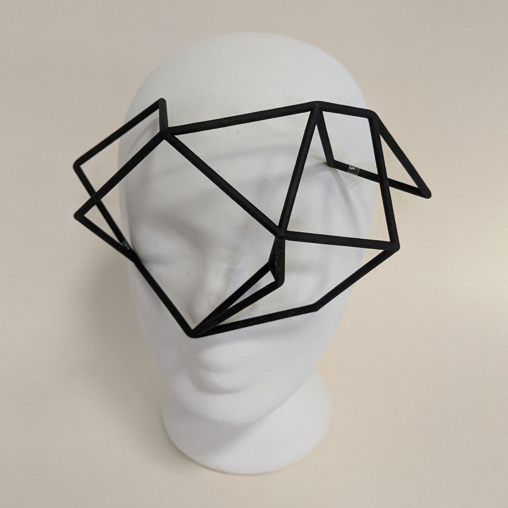 
                  
                    A geometric black frame resembling glasses sits on a white mannequin head, featuring an abstract, polygonal design.
                  
                