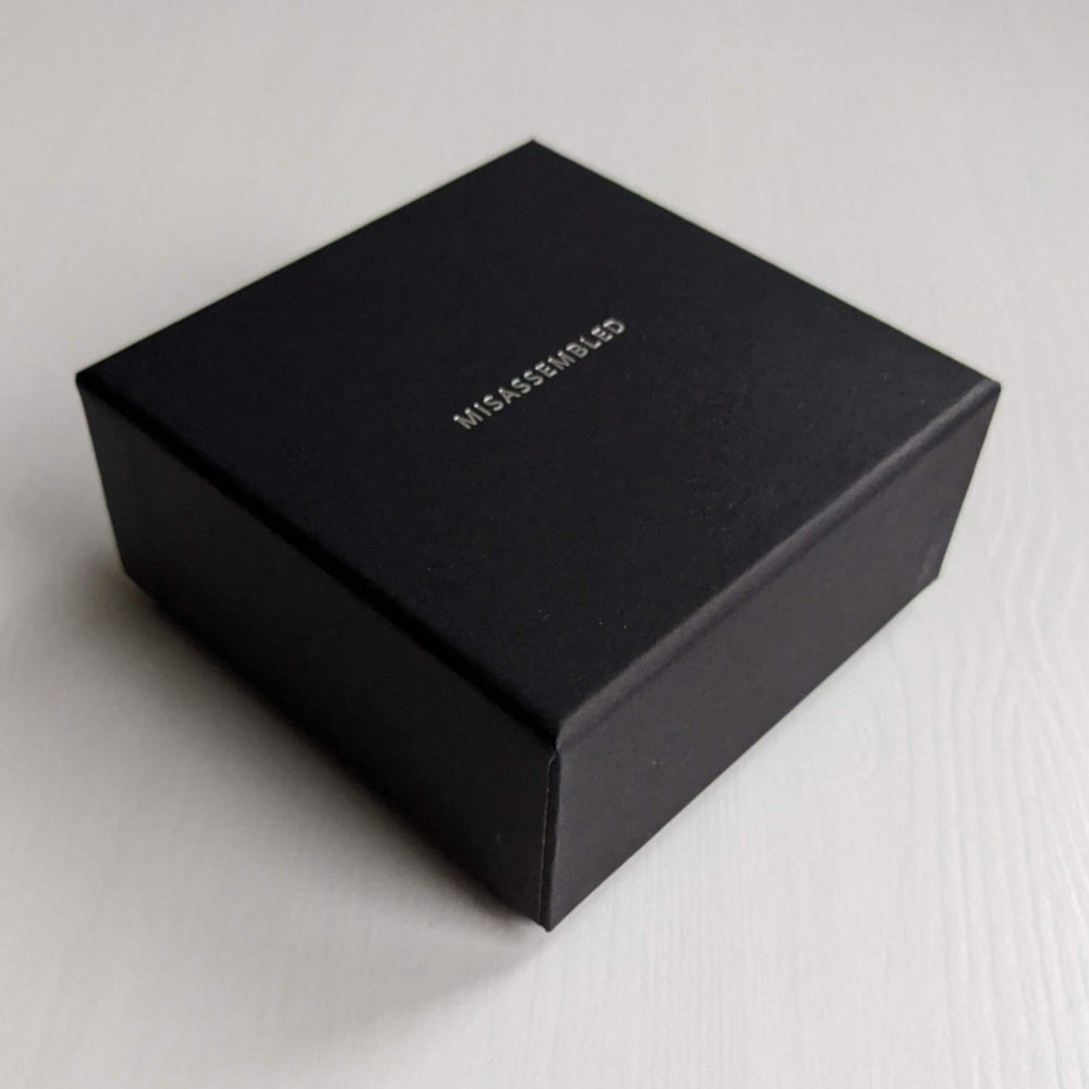 
                  
                    A small black box with the word "MISASSEMBLED" embossed in silver on the top, resting on a light-colored surface.
                  
                