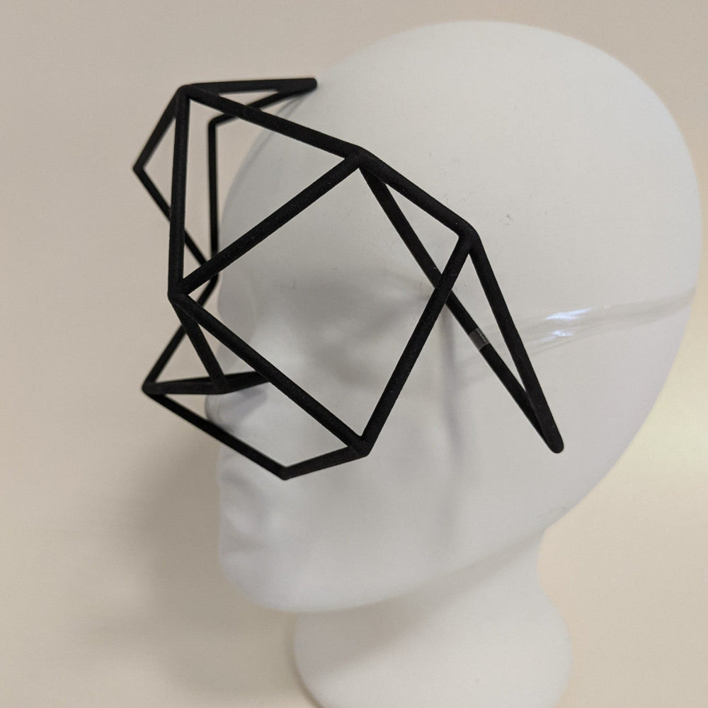 
                  
                    A geometric black frame resembling glasses sits on a white mannequin head, featuring an abstract, polygonal design.
                  
                