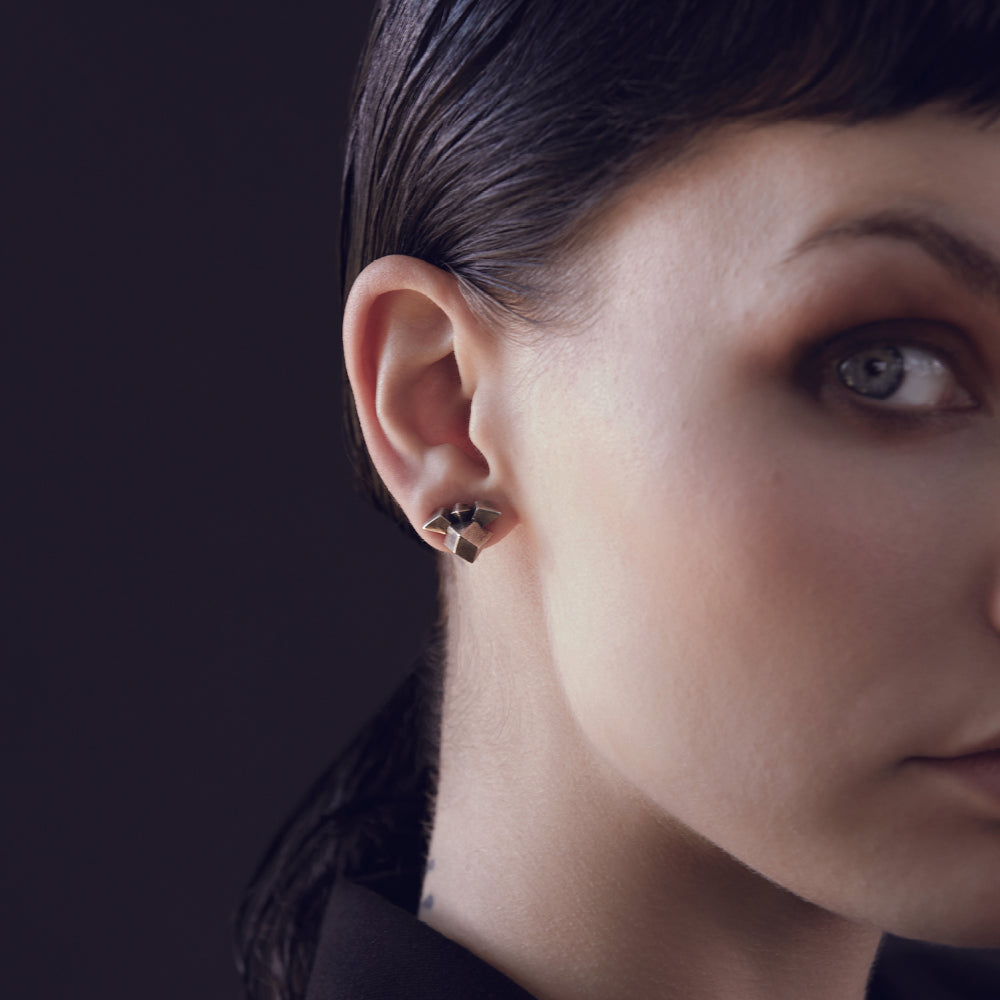 
                  
                    A close-up of a person's ear showcasing a stylish geometric earring against a dark background.
                  
                