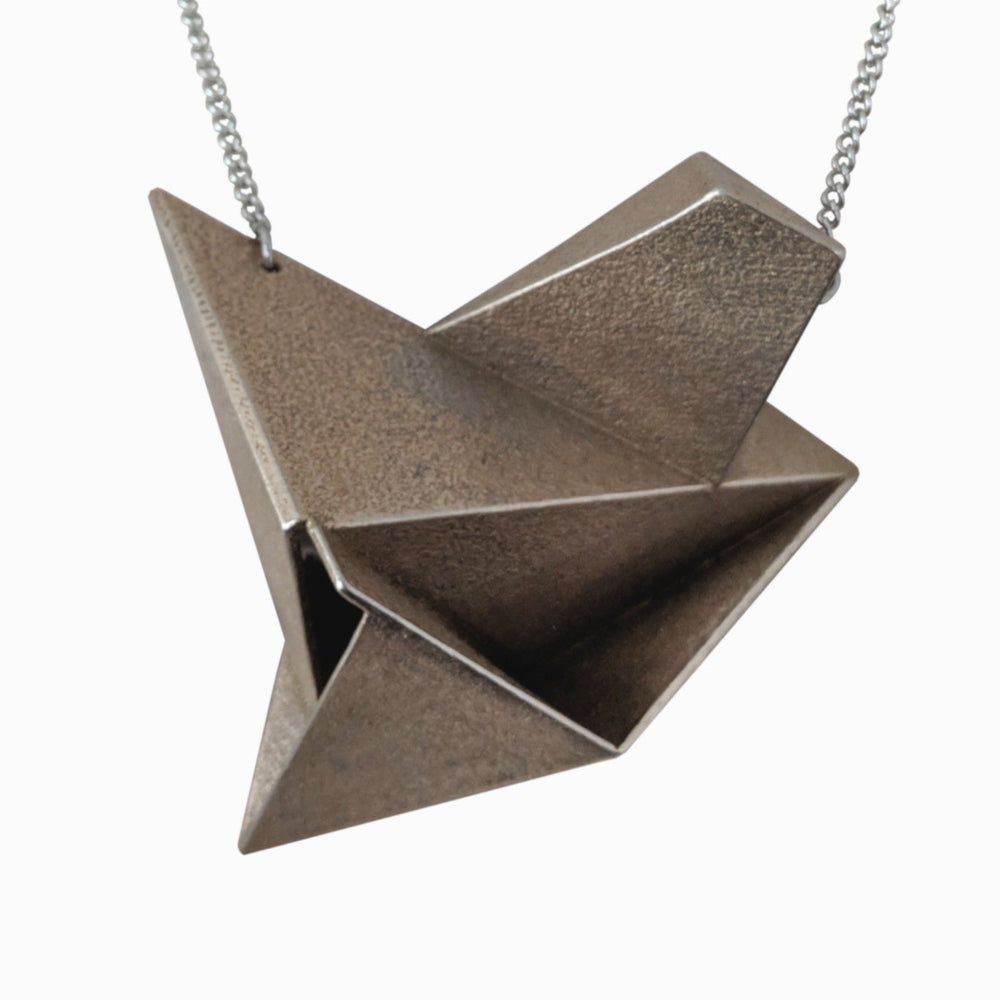 
                  
                    A metallic origami-style pendant in a geometric design, hanging from a delicate chain. The surface has a textured finish.
                  
                
