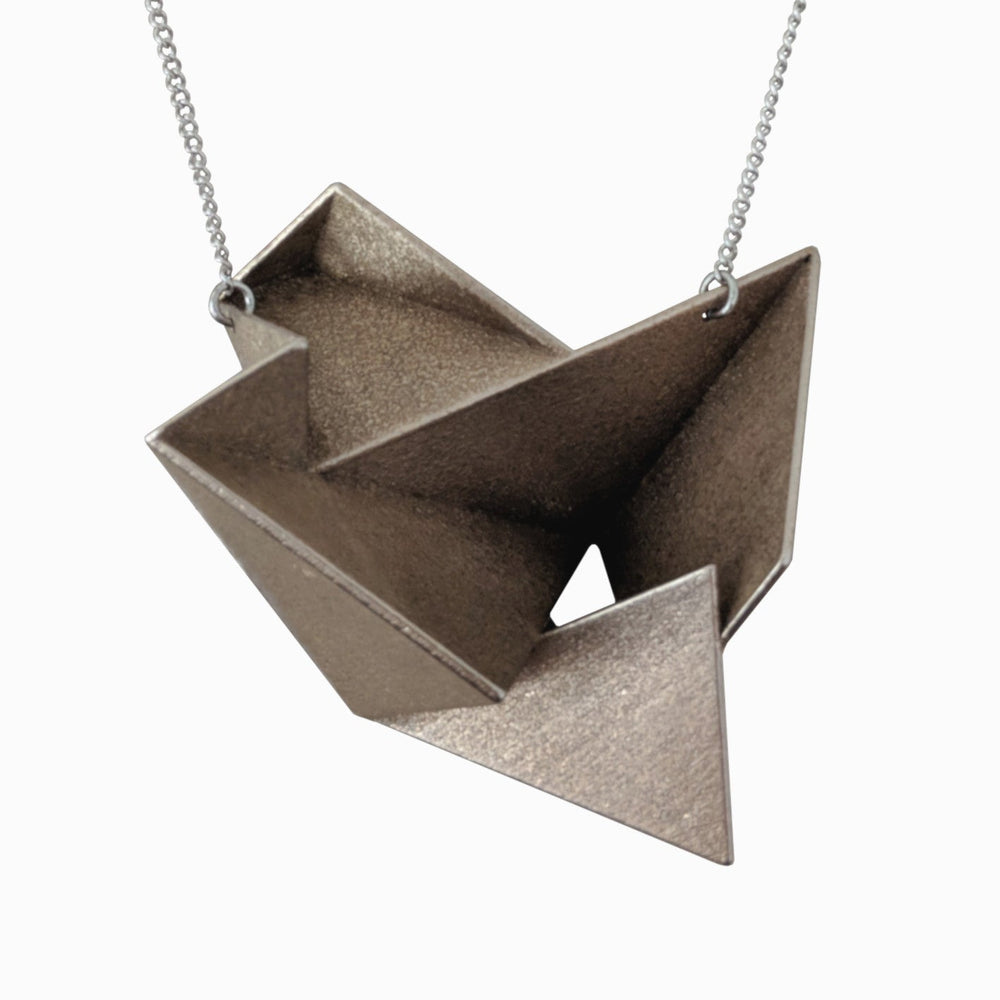 A metallic origami-style pendant in a geometric design, hanging from a delicate chain. The surface has a textured finish.