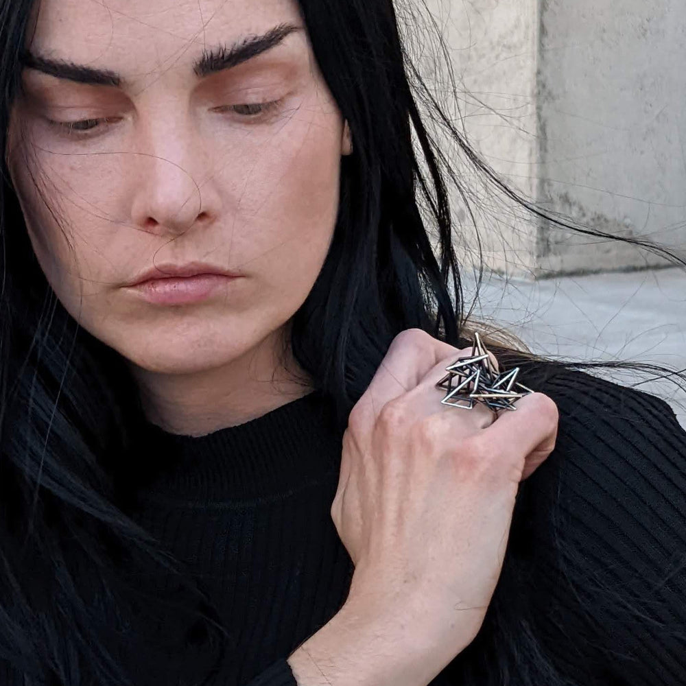 
                  
                    A person with long black hair wears a stylish black ribbed sweater and displays a distinctive silver ring with a geometric design.
                  
                