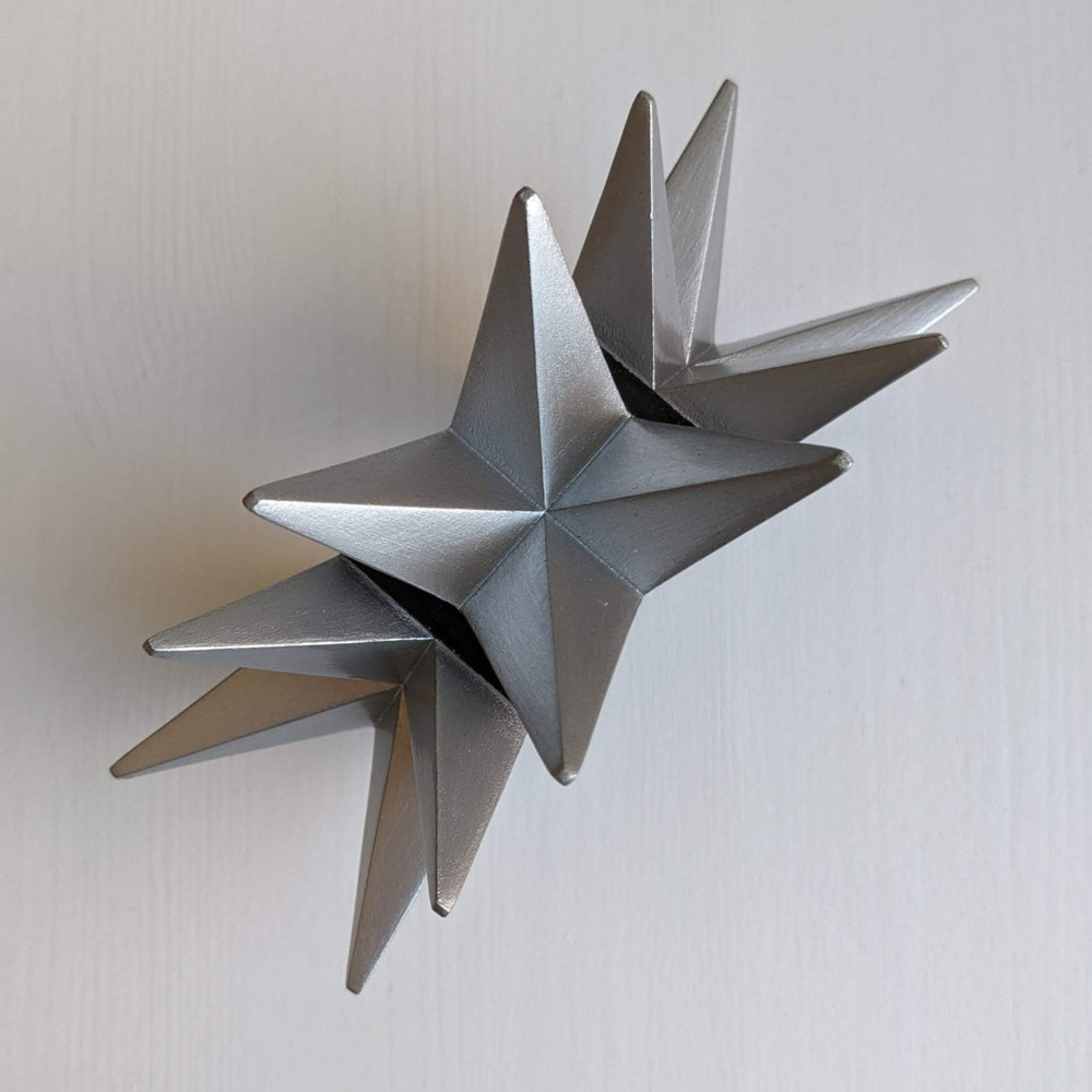 
                  
                    A silver, geometric star sculpture with multiple pointed spikes arranged symmetrically, set against a white background.
                  
                