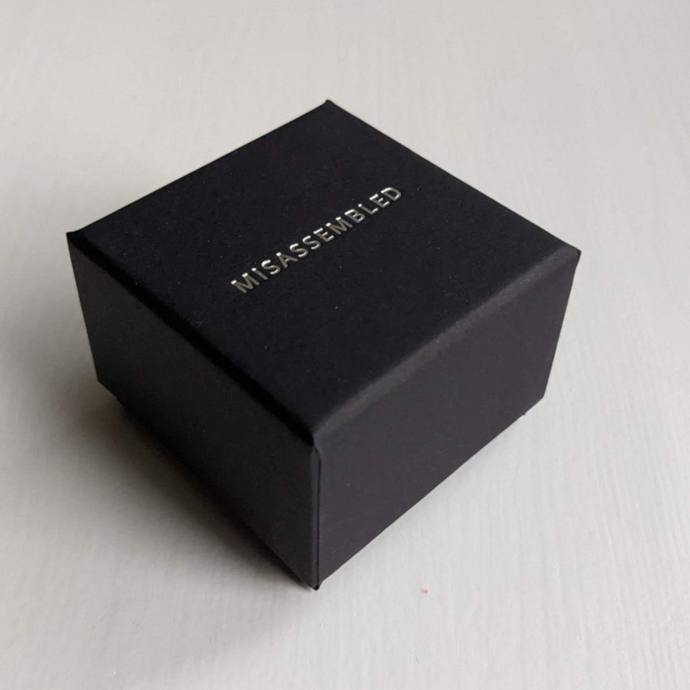 
                  
                    A small black box with the word "MISASSEMBLED" embossed in silver on the top, positioned on a light wooden surface.
                  
                